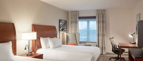 A hotel room with two beds, a desk, a chair, a TV, and a window with curtains.