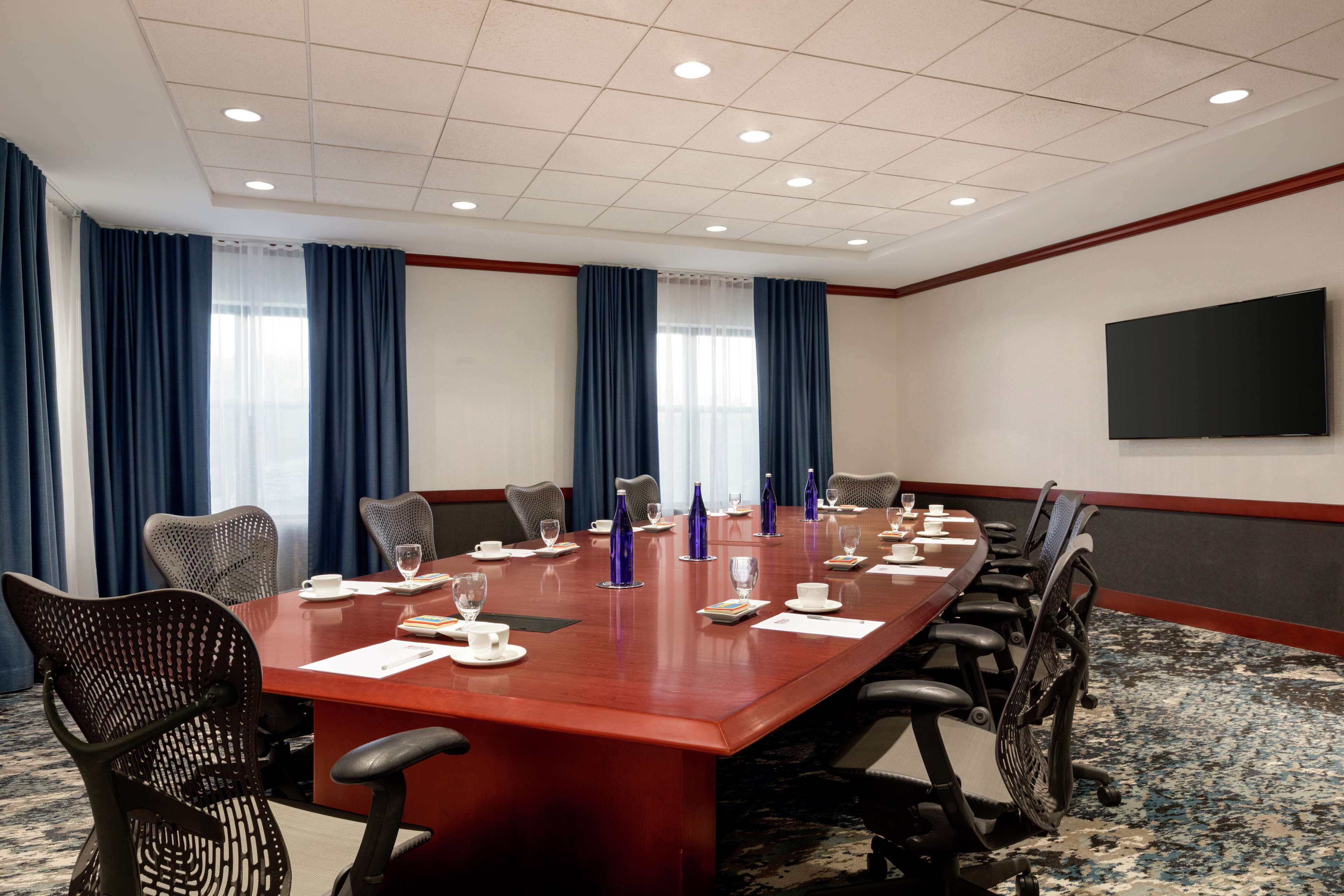 Une salle de conférence avec une longue table, des chaises et un téléviseur à écran plat fixé au mur.