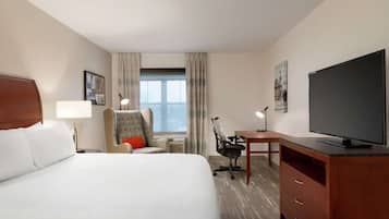 Habitación de hotel con una cama grande, un escritorio, una silla, un televisor y una ventana con cortinas.