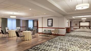 A hotel lobby with round tables, chairs, a coffee table, a patterned carpet, and a large mirror on the wall.