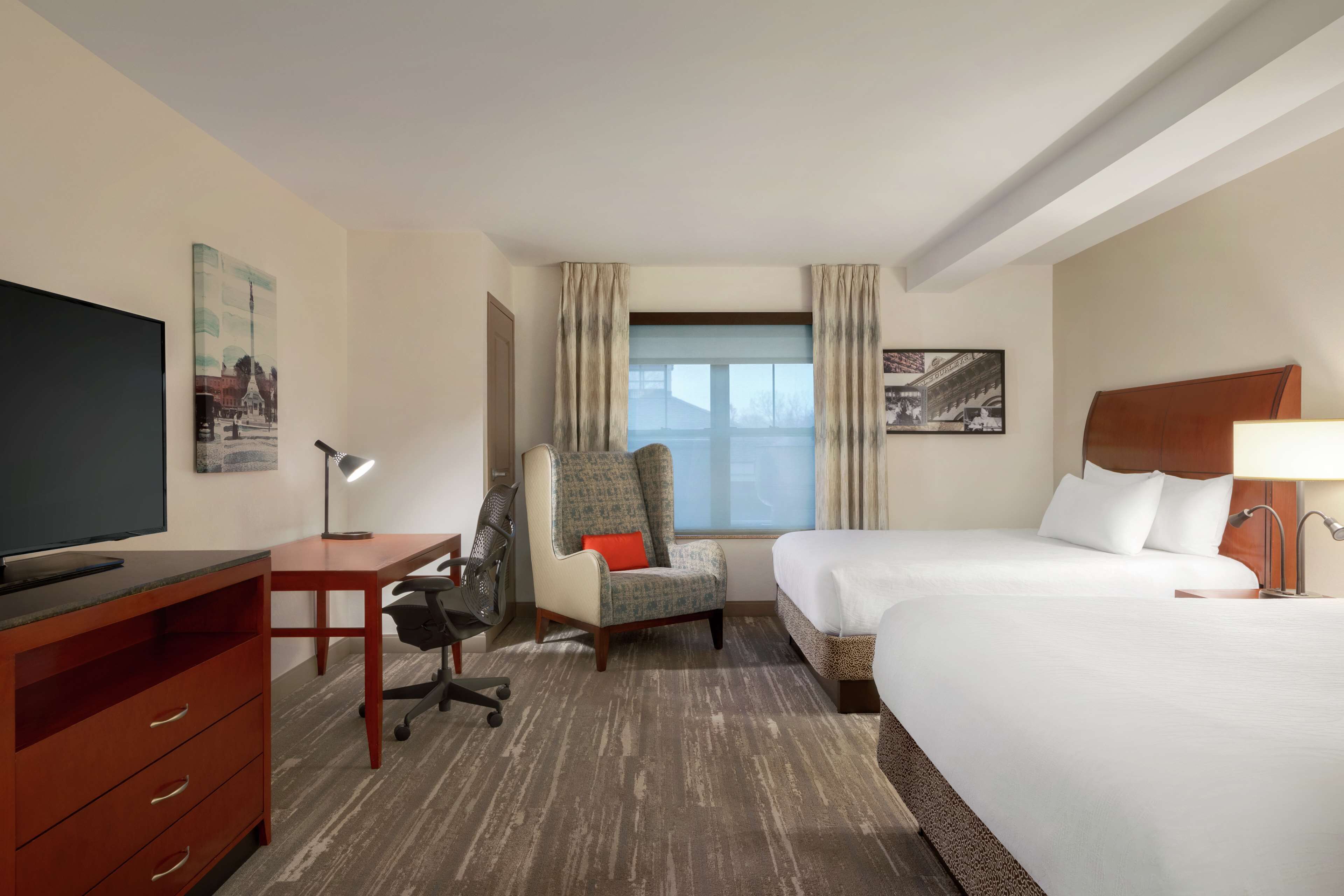 A hotel room with a bed, a desk with a chair, a television, and a window with curtains.
