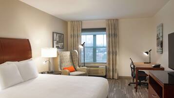 A hotel room with a large bed, a desk, a chair, a TV, and a window with curtains.