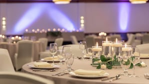 Une table de banquet dressée pour un événement formel, avec des bougies, de la verrerie et des serviettes pliées.