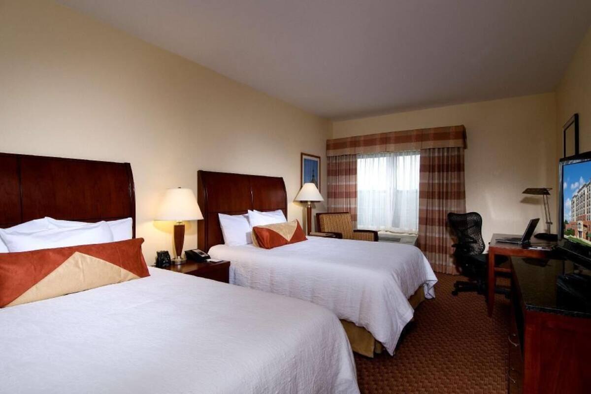 A hotel room with two beds, a desk with a computer, a chair, and a television.