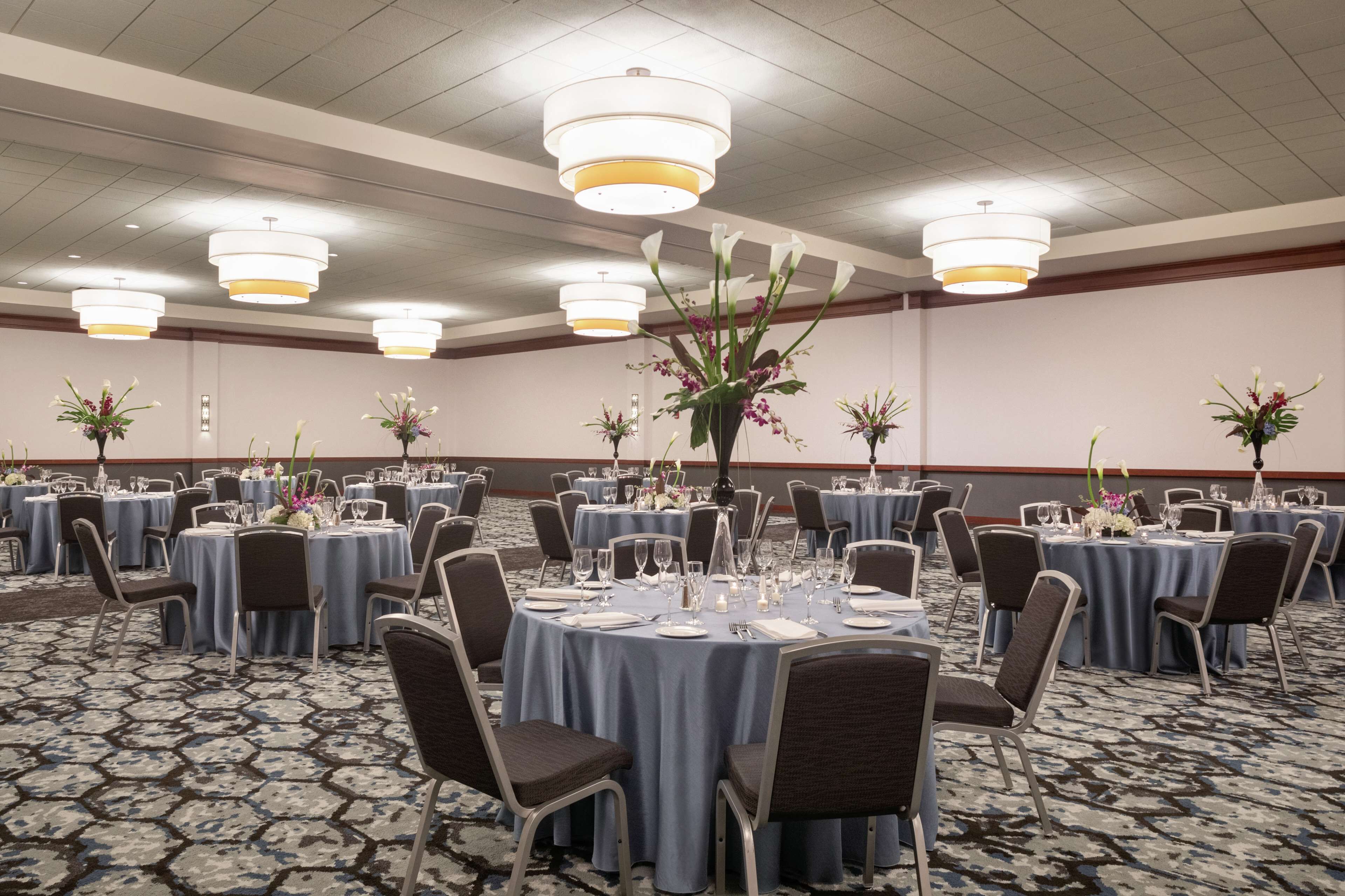 Uma sala de banquetes com mesas redondas, cadeiras e centros de mesa florais.