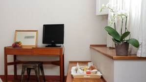 Un escritorio de madera con un televisor, un taburete pequeño, un cuadro enmarco y una bandeja con comida y bebidas.