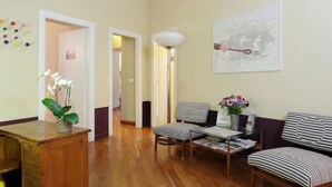 Un salón amplio con suelo de madera, sillones tapizados a rayas, un aparador de madera y una lámpara de pared.