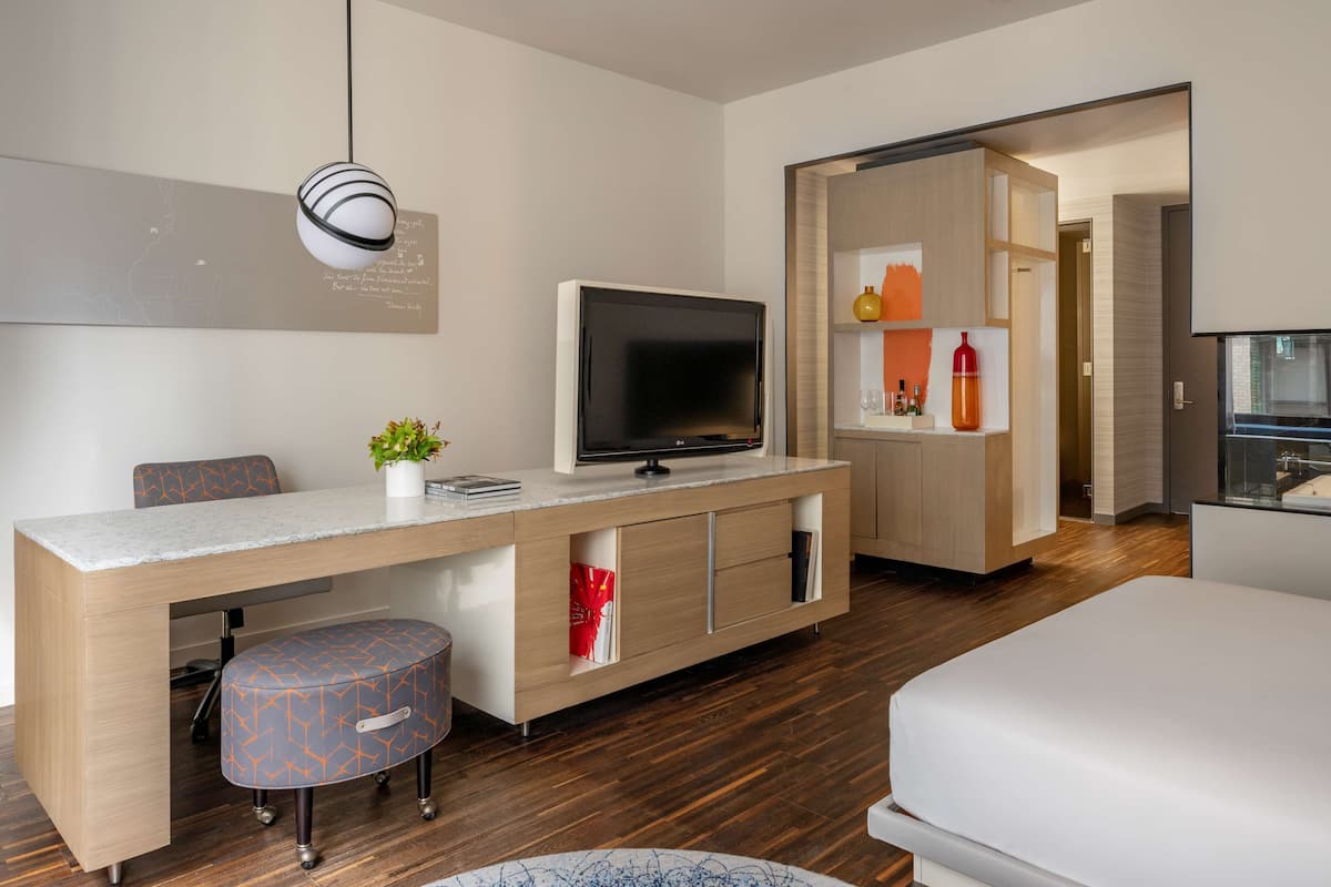 Una habitación de hotel moderna con un escritorio de madera, un televisor de pantalla plana, una cama cómoda y una pequeña zona de estar.