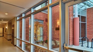 A corridor with large windows, a brick building, and a red pillar outside.