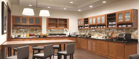 A modern kitchen with wooden cabinets, a central island with bar stools, and overhead pendant lighting.