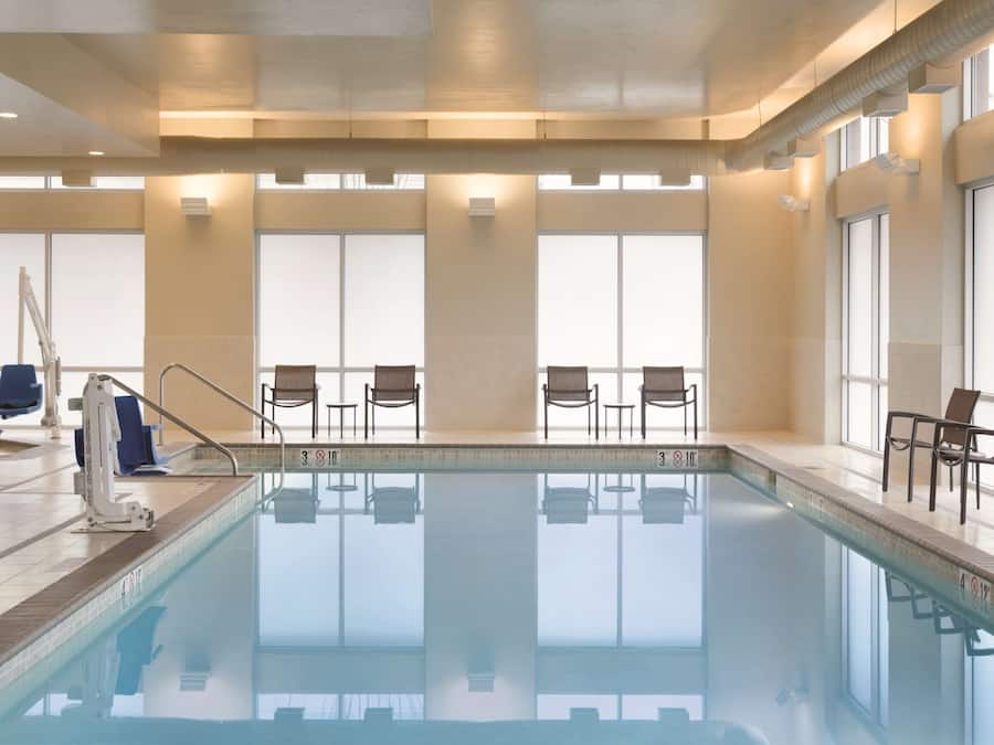 Une piscine avec des chaises et un poste de surveillance pour le sauveteur, de grandes fenêtres et un sol carrelé.