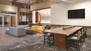 A modern hotel lobby with a large wooden reception desk, comfortable seating areas, and a flat-screen TV mounted on the wall.