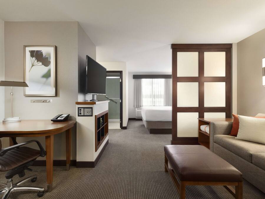 Quarto de hotel com escrivaninha, cadeira, cama e sofá.