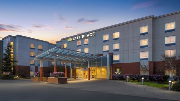 A modern hotel with a glass entrance canopy, a prominent sign, and a landscaped entrance area.