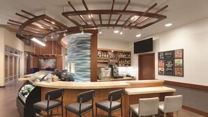 A bar area with a curved counter, bar stools, a coffee machine, and a menu board.
