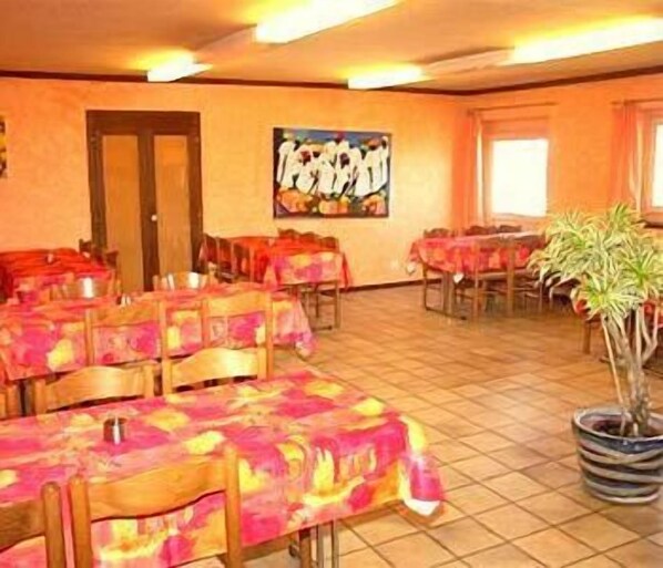 A dining area with multiple tables covered in colorful tablecloths, wooden chairs, and a potted plant. - Hotel La Clef Des Champs (Val-de-Ruz)