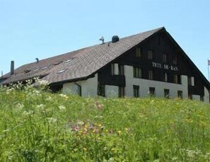 A building with the sign "TITE DE RAN" on its facade, surrounded by a field of wildflowers. - Hotel La Clef Des Champs (Val-de-Ruz)