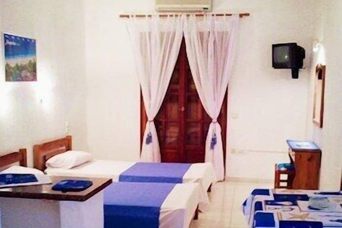 Habitació amb dos llits, una escriptori, una televisió i una finestra amb cortines.