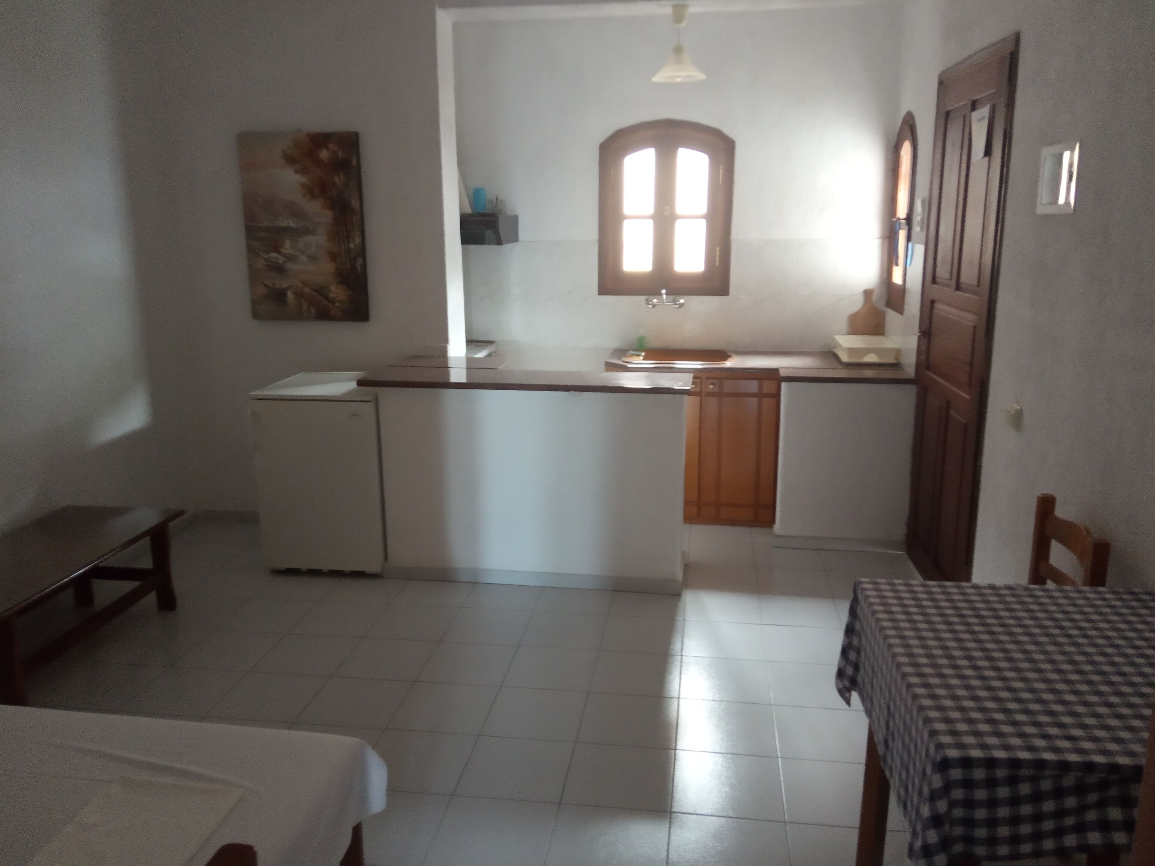 Une cuisine compacte dotée d’un îlot central, d’un petit réfrigérateur et d’une table à manger recouverte d’une nappe à carreaux.