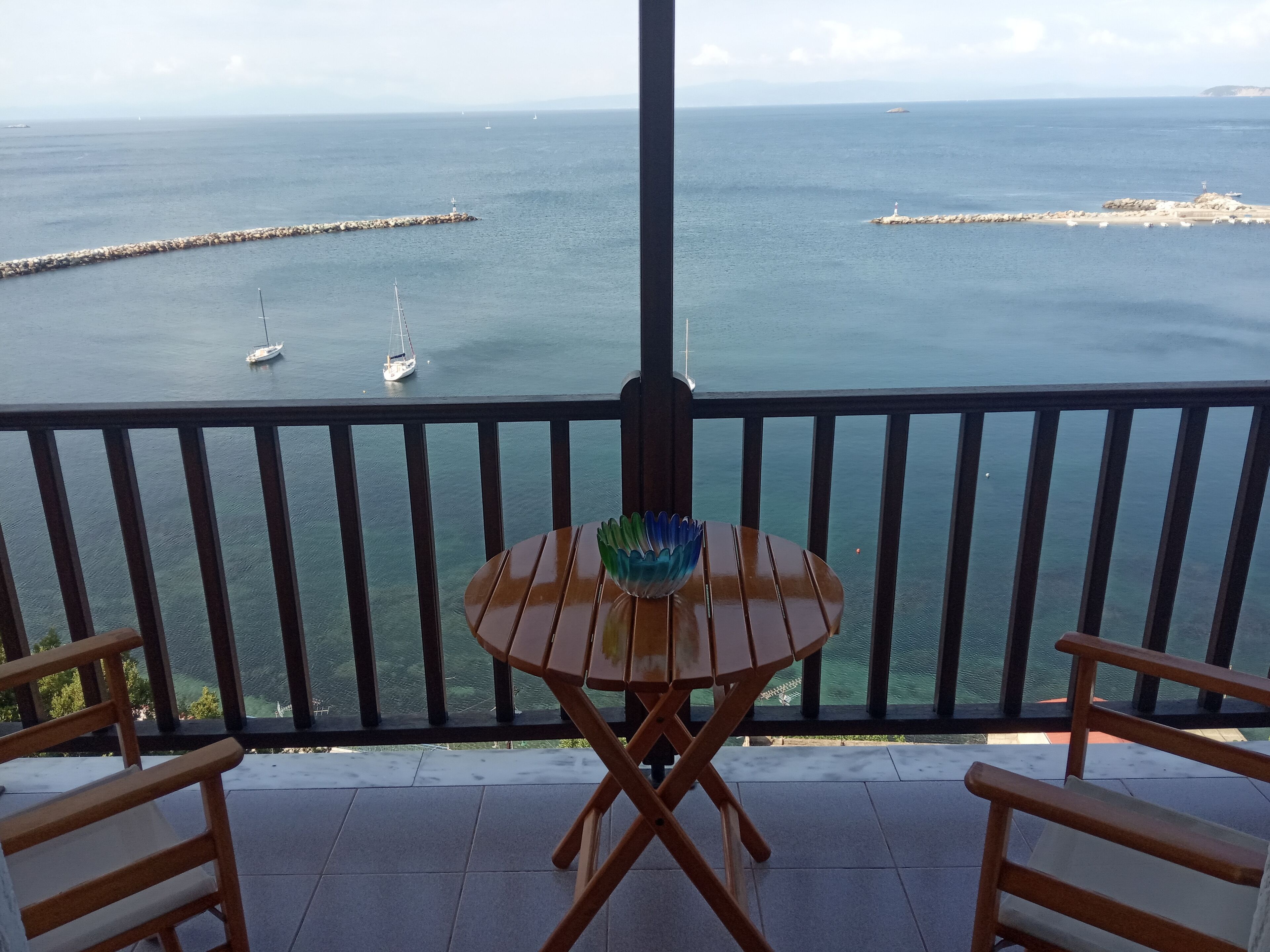 Un balcón con vistas al mar, que incluye una mesa con un centro decorativo y dos sillas de madera.