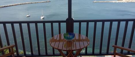 Un balcón con vistas al mar, que incluye una mesa con un centro decorativo y dos sillas de madera.