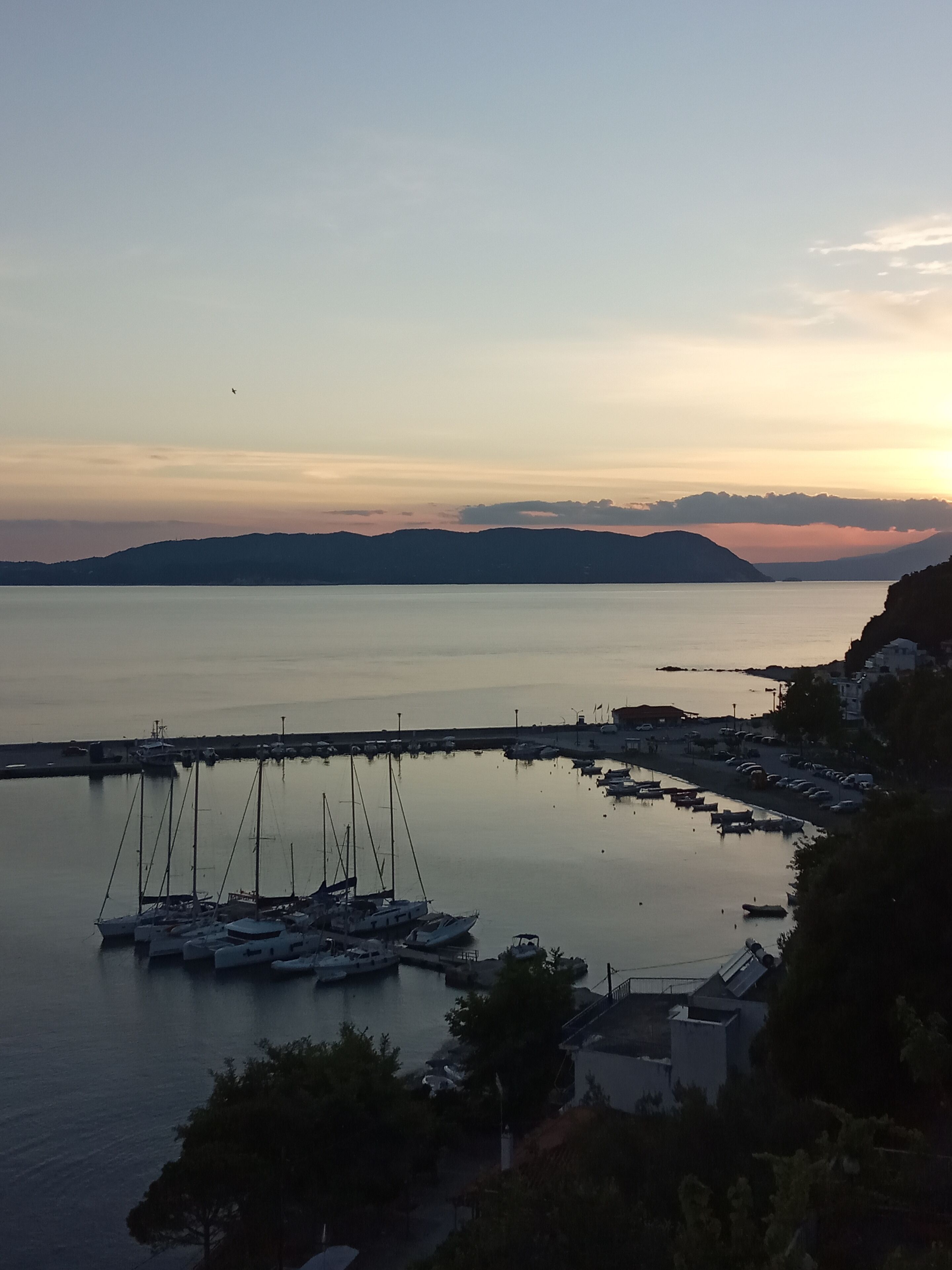 Una marina con barche ormeggiate, acque calme e un paesaggio collinare sullo sfondo.