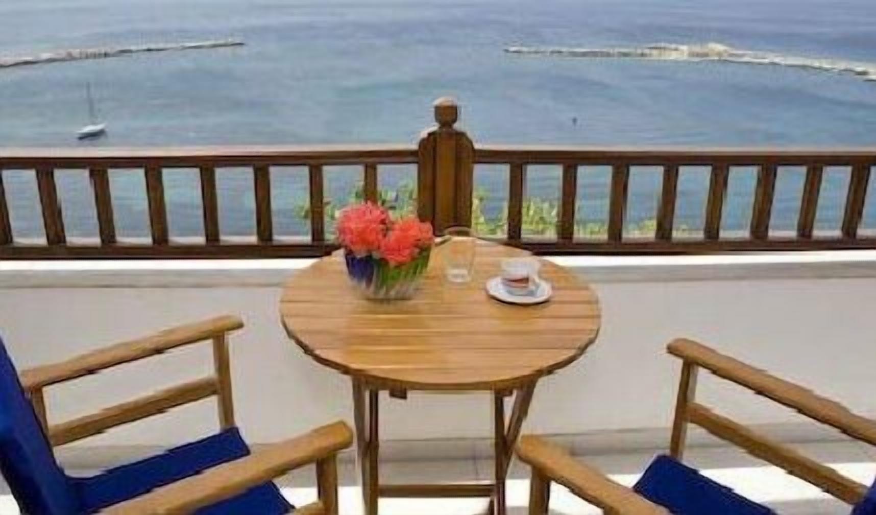A wooden table with two chairs on a balcony overlooking the sea.