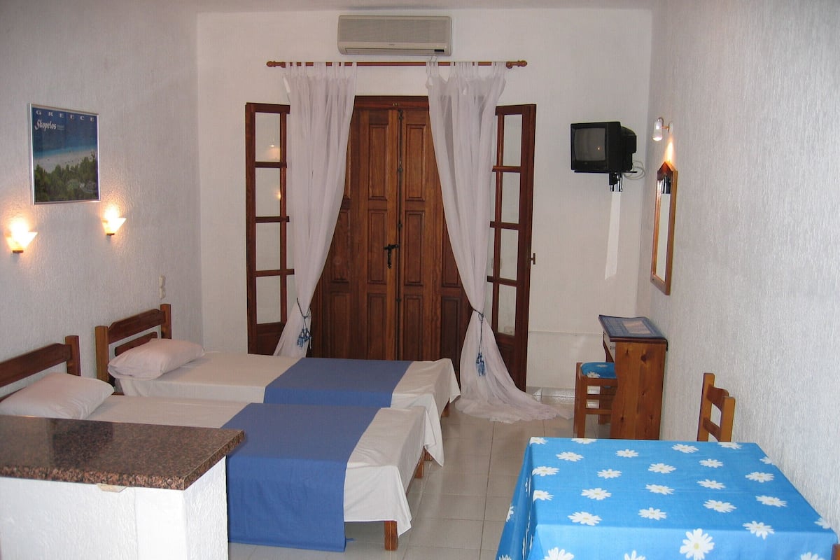 Una habitació amb dos llits, una taula, una cadira, un televisor i un cartell a la paret.
