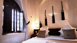 A hotel room with a large bed, a window with curtains, and a wall-mounted lamp. - Riad Dar El Grably (Marrakech)