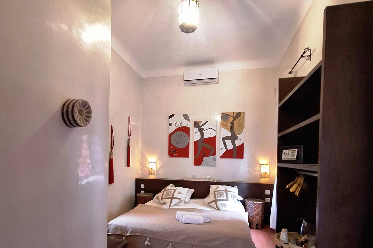 Una habitación de hotel ordenada con cama, mesitas de noche, una pequeña mesa redonda y decoración en la pared.