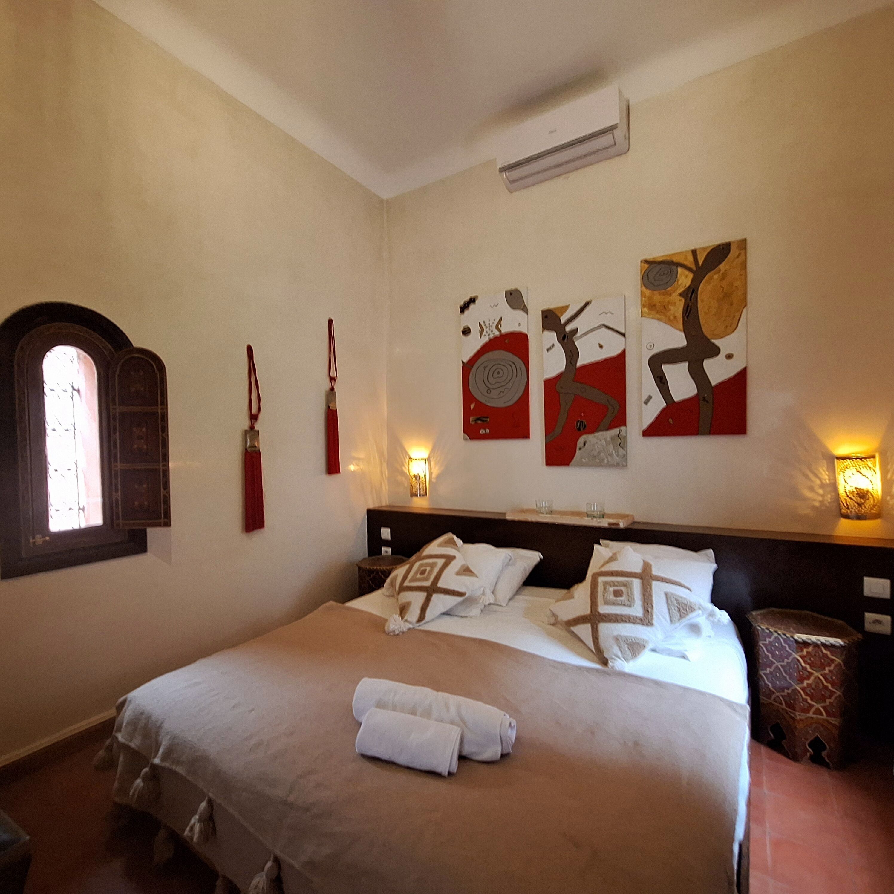 Quarto de hotel com uma cama grande, janela com vista e três obras de arte penduradas na parede.