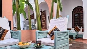 A traditional Moroccan-style outdoor seating area with two light blue sofas, a glass table with a bowl of fruit, and a candle. - Riad Dar El Grably (Marrakech)
