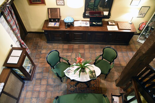 A reception area with a wooden desk, two green chairs, a small table with a plant, and a patterned rug.