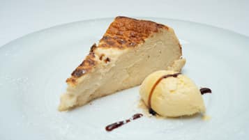 Una porción de pastel de queso con una bola de helado de vainilla sobre un plato blanco.