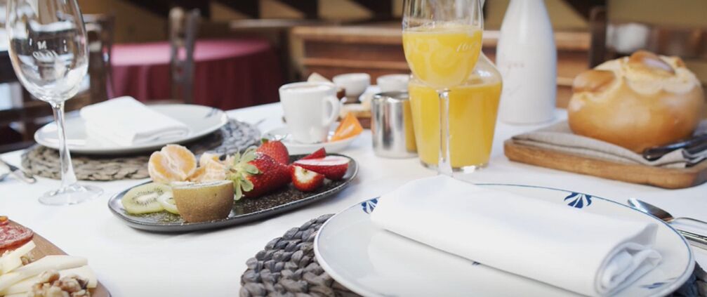 A breakfast setting with a plate of fruit, a glass of orange juice, and a loaf of bread on a table.