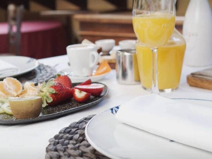 A breakfast setting with a plate of fruit, a glass of orange juice, and a loaf of bread on a table.