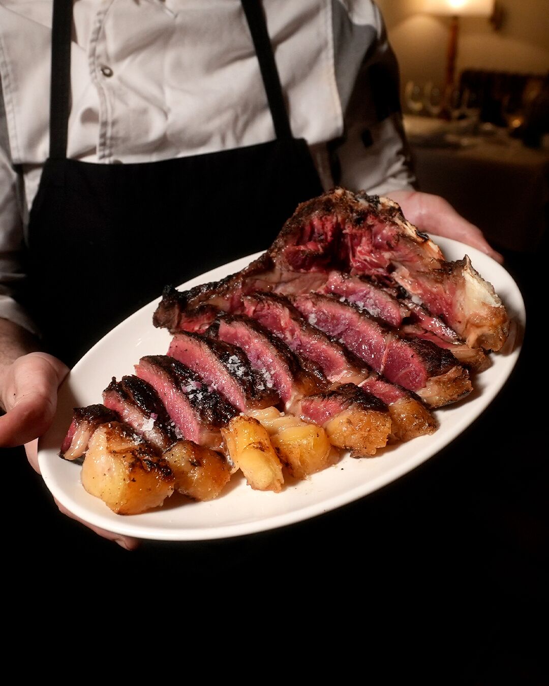 A person holding a plate with sliced steak and roasted potatoes.