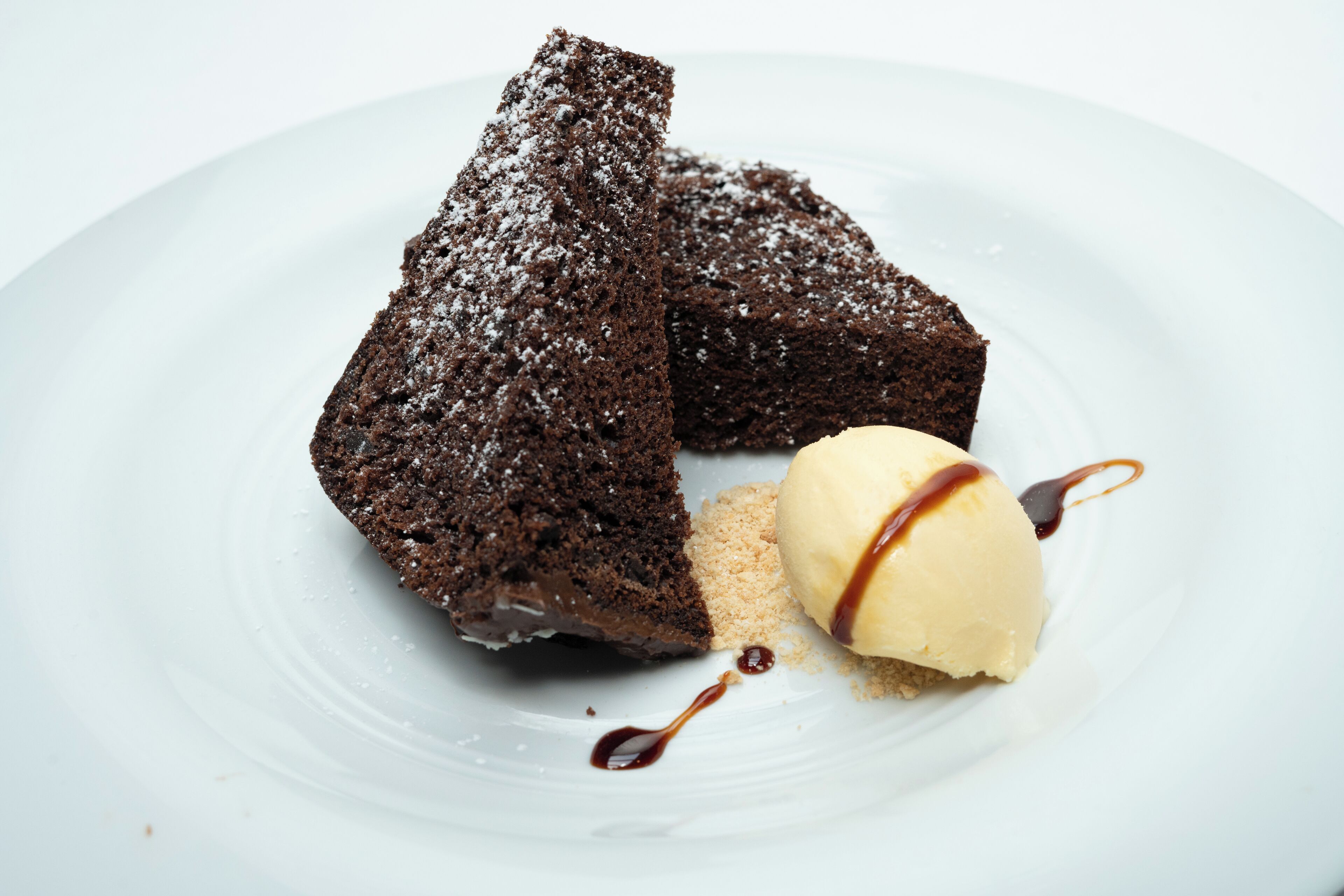 Un plato de postre con un brownie y una bola de helado de vainilla, ambos espolvoreados con azúcar glas.