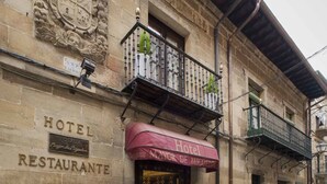 A historic building with a stone facade, a balcony with plants, and a sign reading "Hotel Posada Restaurante."