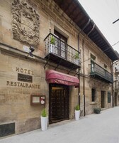 A historic building with a stone facade, a balcony with plants, and a sign reading "Hotel Posada Restaurante."