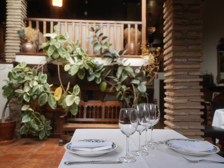Taula de menjador coberta amb plats, coberts i gots de vi, envoltada de plantes en testos i un pilaret de maó.