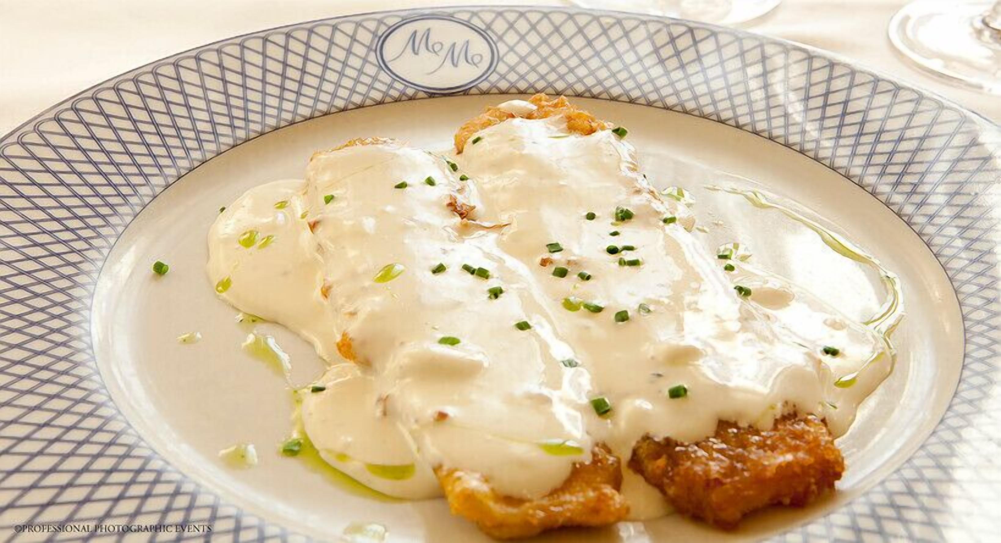 A plate of food with a creamy sauce and green garnish on a patterned plate.