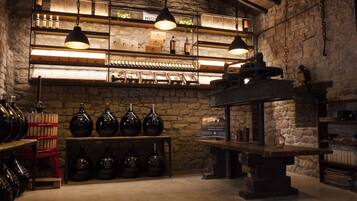 A rustic interior with stone walls, shelves displaying wine bottles, and hanging lights.