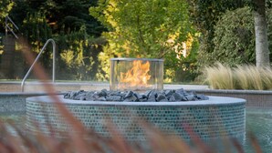 A circular pool with a glass fire feature in the center, surrounded by rocks and a tiled edge. - Spirit Hotel Thermal Spa (Sarvar)