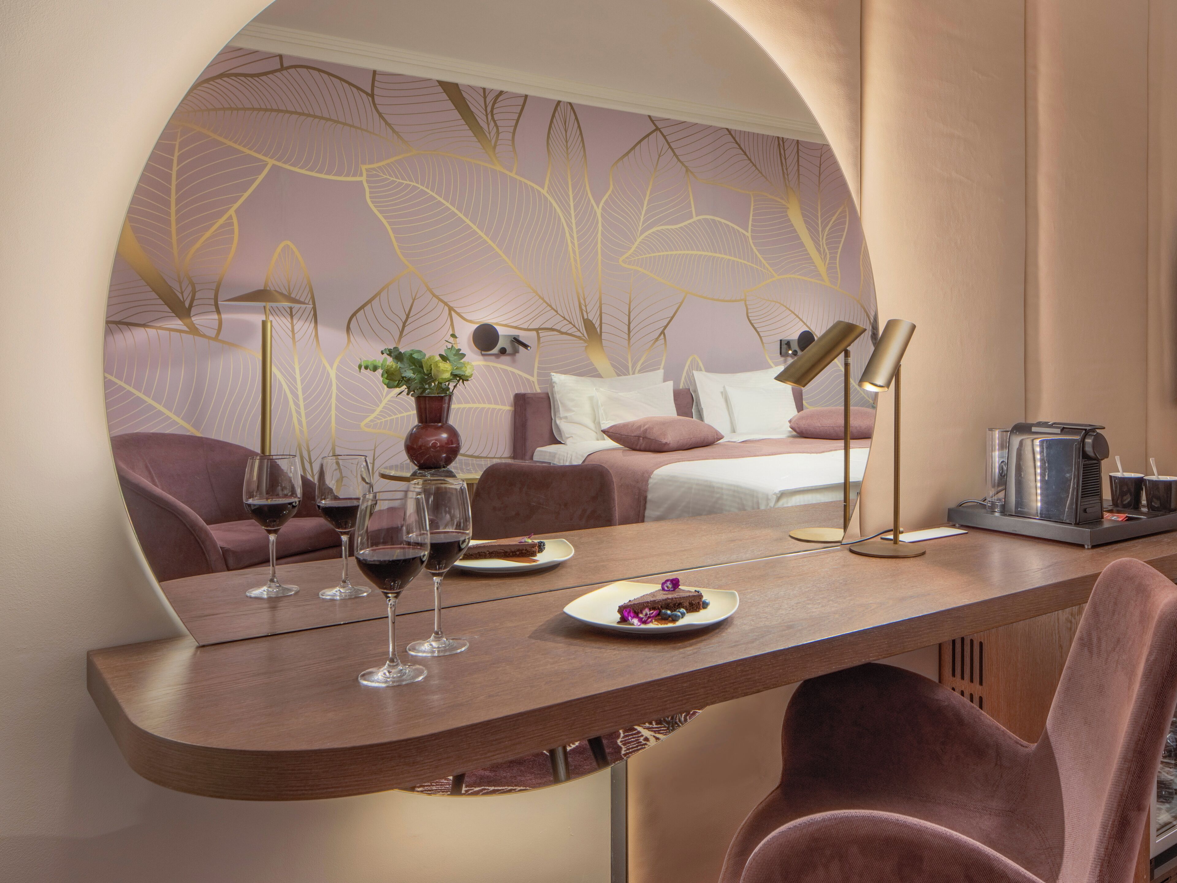 A modern hotel room with a curved dining table, a sofa, a bed with a headboard, and a coffee machine.