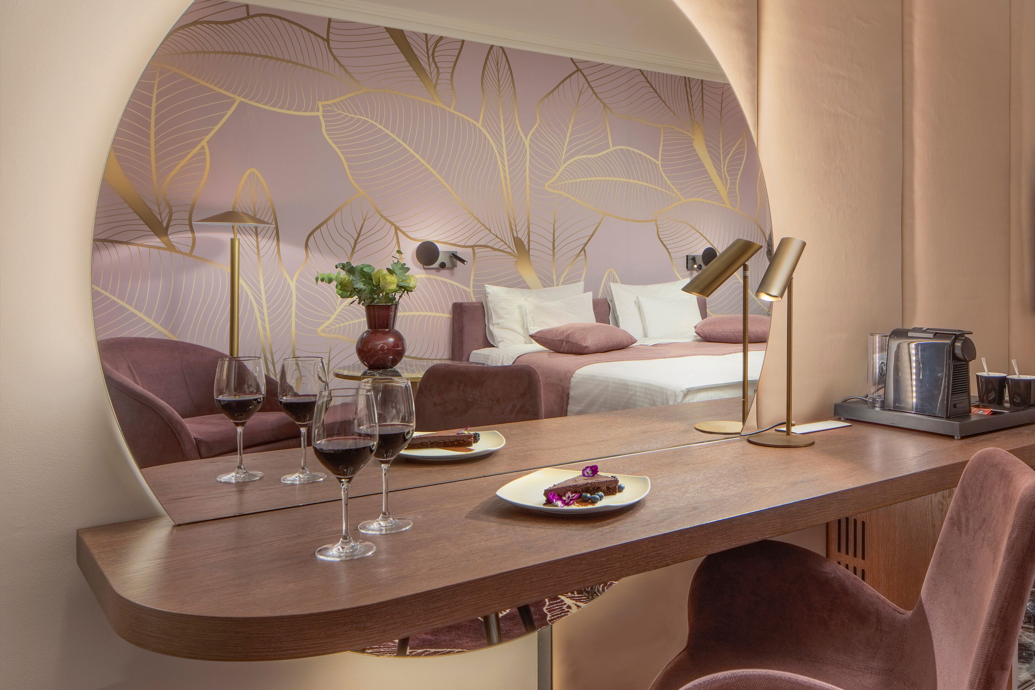 A modern hotel room with a curved wooden table, a sofa, and a bed with a leaf-patterned wall.