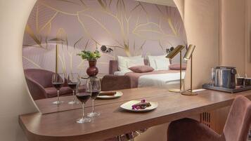 A modern hotel room with a curved wooden table, a sofa, and a bed with a leaf-patterned wall.