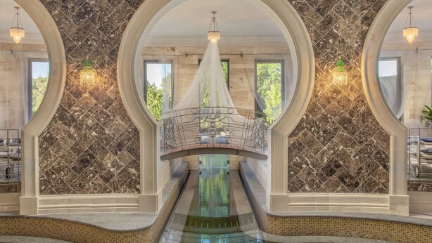 A luxurious indoor pool area with a central water feature, marble walls, and a decorative bridge. - Spirit Hotel Thermal Spa (Sarvar)