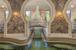 A luxurious indoor pool area with a central water feature, marble walls, and a decorative bridge. - Spirit Hotel Thermal Spa (Sarvar)