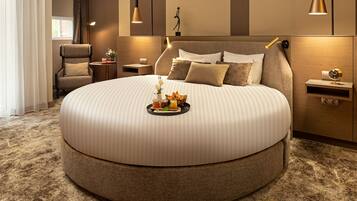 A round bed with a tray of food, a chair, bedside tables, and wall-mounted lamps in a modern hotel room.